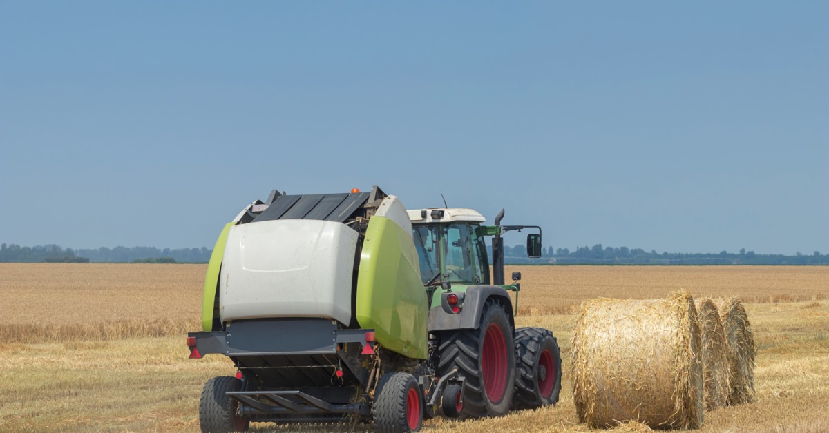 A rear view of a tractor towing a green round hay baler in a field with three round hay bales next to it.